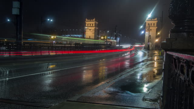 Lapso-de-tiempo-noche-de-ocupado,-mojada-la-calle-con-un-estadio-nacional-en-Varsovia-de-fondo