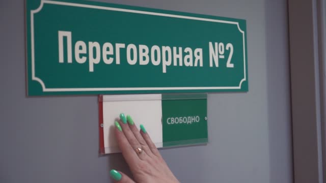 Woman-hand-moves-plate-to-occupied-on-door-with-cyrillic-text-meeting-room
