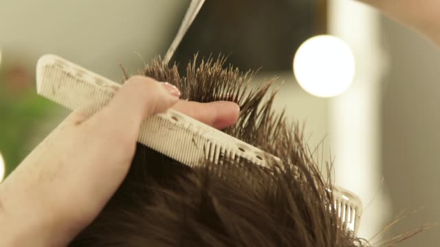 Hands-hairstylist-cutting-hair-with-scissors-and-combing-close-up.-Haircutter-making-male-hairstyle-with-professional-scissors-and-comb-in-beauty-salon