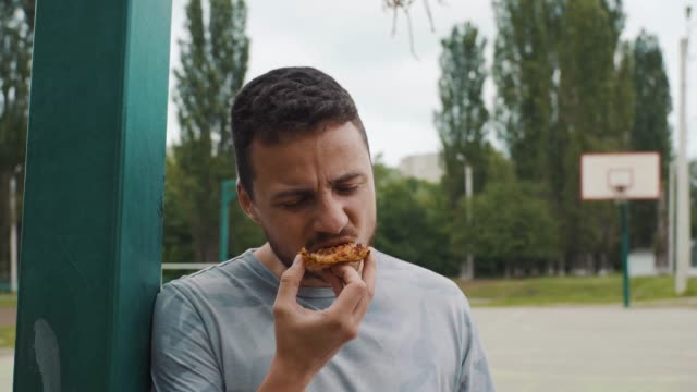 Close-up-of-handsome-man-eating-pizza-on-a-basketball-court
