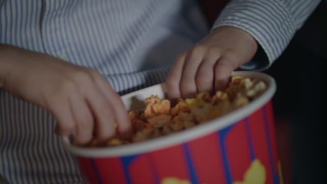 Child-hand-taking-popcorn-from-paper-box-at-cinema.-Kids-take-caramel-popcorn