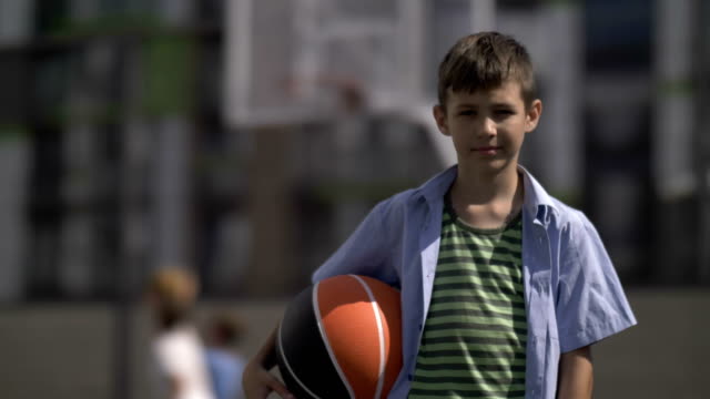 Retrato-de-un-niño-con-una-pelota-de-baloncesto-en-una-cancha-de-baloncesto,-mira-a-la-cámara