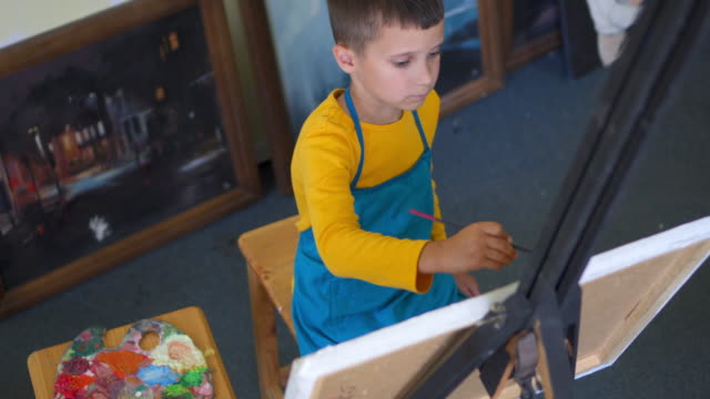 Niño-creativo-que-sumerge-el-pincel-en-pintura-y-dibujo-sobre-tela