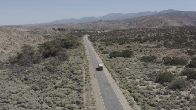 Einen-gelben-amerikanischen-Schulbus-fahren-auf-einer-Straße-in-der-kalifornischen-Wüste-Sandy
