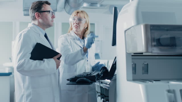 Two-Research-Scientists-Programm-Medical-Equipment-with-Computer-Keyboard.-Team-of-Professionals-Doing-Pharmaceutical-Research-in-Modern-Laboratory