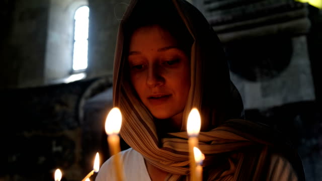 Frau-in-ein-Kopftuch-stellt-eine-Kerze-und-betet-vor-der-Ikone-in-der-orthodoxen-katholischen-Kirche