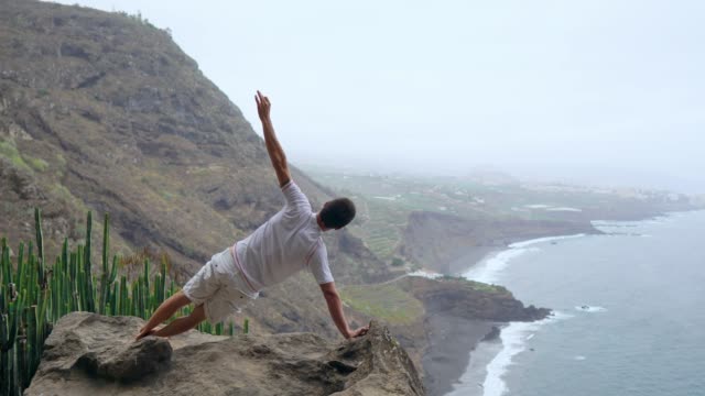 Un-hombre-de-pie-en-una-mano-en-las-montañas-de-espaldas-a-la-cámara-mirando-al-mar-y-meditar-en-las-Islas-Canarias.