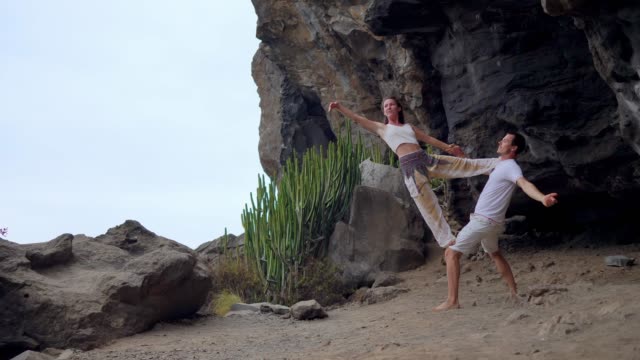 Ein-Mann-und-eine-Frau-stehen-am-Rand-einer-Klippe-mit-Blick-auf-den-Ozean-erheben-ihre-Hände-oben-und-atmen-Sie-die-frische-Seeluft-während-yoga