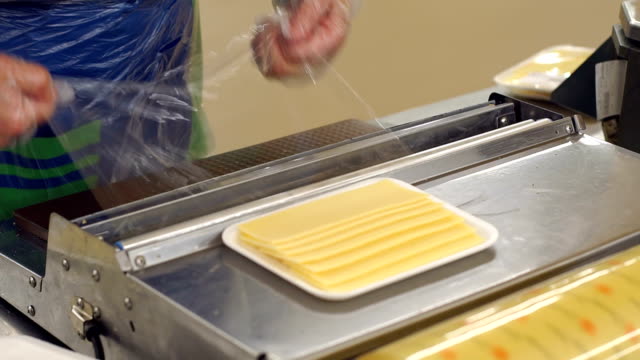 Saleswoman-slicing-cheese-in-a-supermarket-and-wrapping-it-in-cling-film.