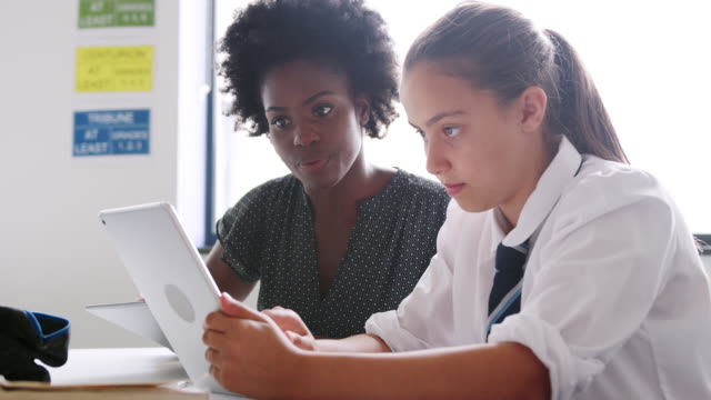Weibliche-High-School-Lehrer-mit-Digital-Tablette-geben-Studentin-tragen-einheitliche-Einzelunterricht-am-Schreibtisch