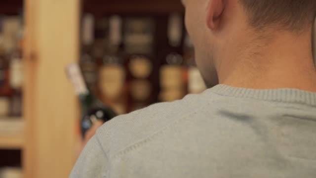 Man-takes-and-puts-back-wine-bottle-closeup-Customer-is-choosing-drink-in-alcohol-shop