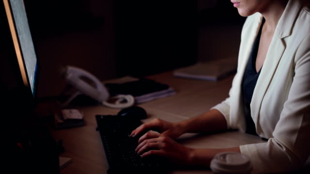 Incline-para-arriba-tiro-de-serio-joven-trabajando-en-la-computadora-escribiendo-y-mirando-la-pantalla-sentado-en-la-mesa-de-trabajo-solo-en-oficina-oscuro-por-la-noche.-Concepto-de-tecnología-y-trabajo.