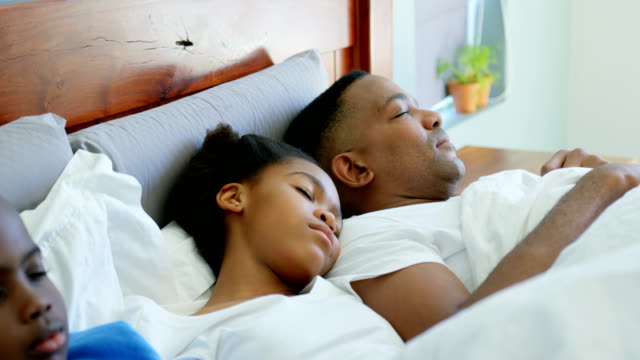 Vista-frontal-de-la-familia-negro-durmiendo-juntos-en-la-cama-en-dormitorio-de-casa-confortable-4k