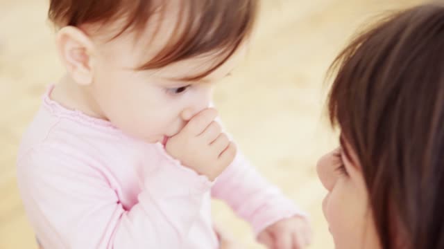 Close-up-of-loving-young-mother-playing-with-her-cute-baby-girl-with-big-brown-eyes-sucking-her-thumb