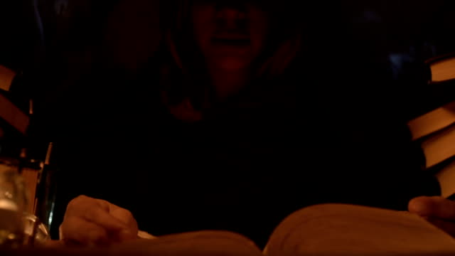Close-up-girl-magician-in-the-hood-in-a-dark-room-by-candlelight-reads-a-spell.-Low-key-live-camera.-Mystic.