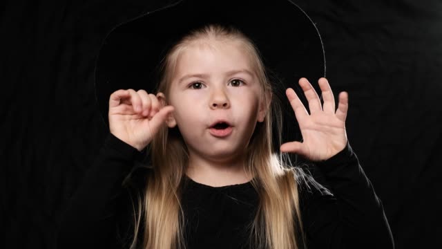 Kleine-hübsche-Mädchen-Hexe-in-schwarzem-Kleid-und-Hut-schreien-auf-dunklen-Hintergrund