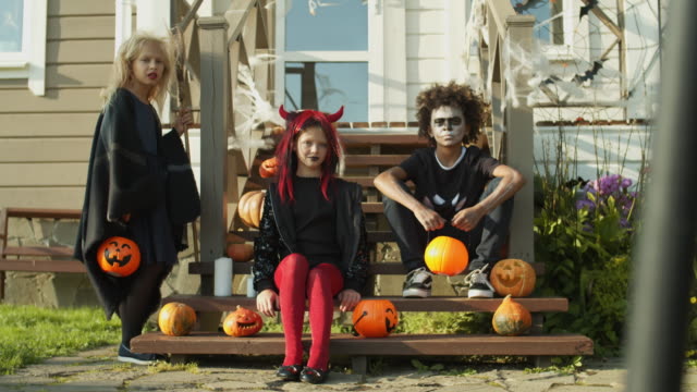 Drei-Kinder-in-Halloween-Kostümen-sitzen-auf-Veranda