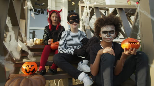 Three-Teenagers-Wearing-Halloween-Costumes-Sitting-on-Porch