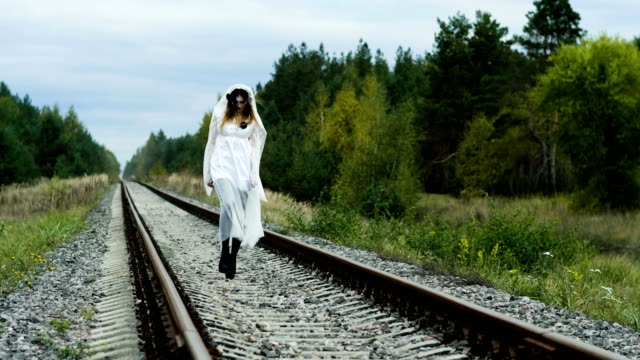 A-woman-with-make-up-of-dead-bride-for-Halloween-in-wedding-gown-on-the-rails.-4K