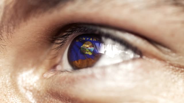 Mann-mit-braunem-Auge-aus-nächster-Nähe,-die-Flagge-des-Montana-Staates-in-Iris,-vereinigte-Staaten-von-Amerika-mit-Windbewegung.-Videokonzept
