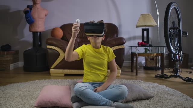 Young-Caucasian-teen-with-curly-hair-in-VR-headset-holding-remote-control-and-looking-around.-Child-using-virtual-reality.-Augmented-reality,-VR-glasses,-generation-Z.-Cinema-4k-ProRes-HQ.