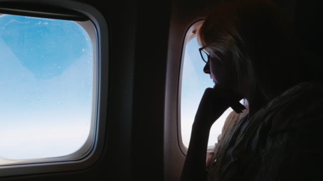 Eine-Frau-in-Gläsern-befasst-sich-mit-dem-Flugzeugfenster.-Silhouette,-Seitenansicht