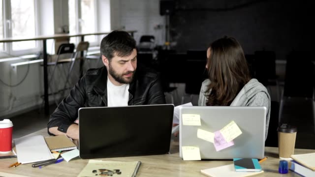 Young-office-workers-arguing-in-front-of-their-laptops.-Woman-showing-papers-being-very-angry.-Slowmotion