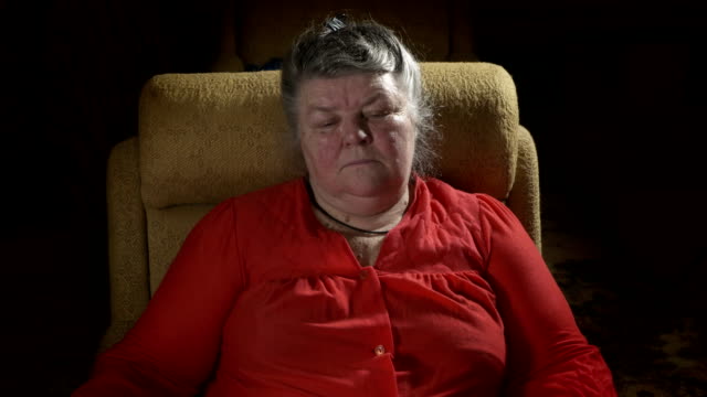 Eine-ältere-Frau-Fett-sitzt-im-Sessel-vor-dem-Fernseher-in-einem-dunklen-Raum-zu-Hause