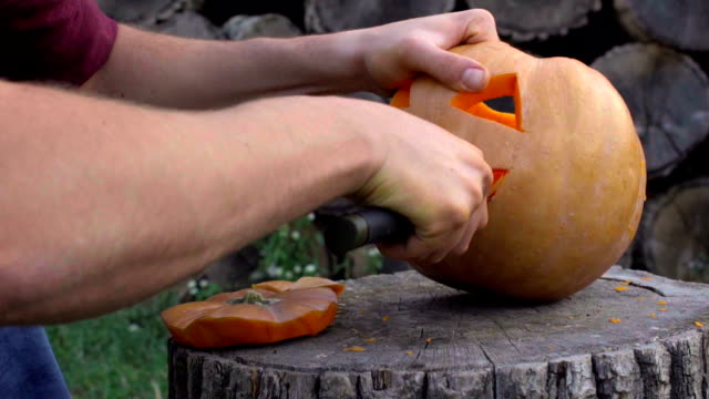 Man-carves-from-a-pumpkin-Jack-o'-lantern-in-the-backyard-on-a-tree-stump