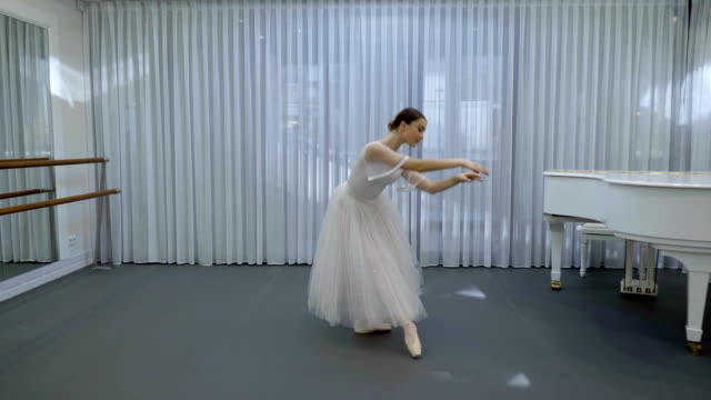 Ballerina-in-long-ballet-tutu-dances-in-studio-with-white-grand-piano
