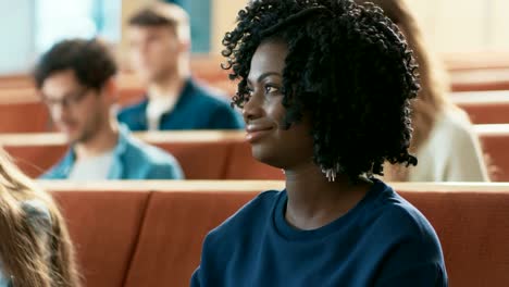 Close-up-an-einer-schönen-schwarzen-Studentin-unter-ihren-Kommilitonen-im-Klassenzimmer-sitzen,-schreibt-sie-in-der-Arbeitsmappe-und-hört-einen-Vortrag.