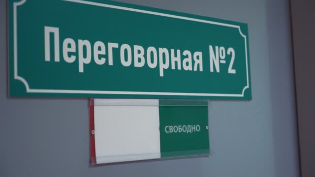 Female-hand-moves-plate-to-occupied-on-door-with-cyrillic-text-meeting-room