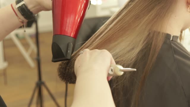 Hairstylist-drying-female-hair-after-hairdressing-in-beauty-salon.-Close-up-haircutter-styling-long-hair-with-dryer-and-hairbrush-after-washing-and-cutting.-Finish-hairdressing-in-beauty-salon