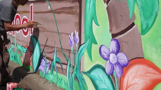 Mural-painter-paints-a-garden-image-in-color-on-the-school-wall.-time-lapse