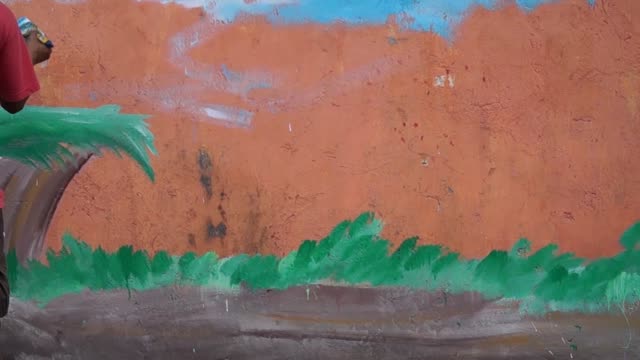 Mural-painter-paints-a-garden-background-image-in-color-on-the-school-wall.-time-lapse