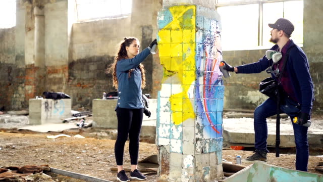 Slow-motion-of-creative-graffiti-painters-partners-decorating-abandoned-house-with-beautiful-images-using-bright-aerosol-paint.-Teamwork,-young-people-and-art-concept.