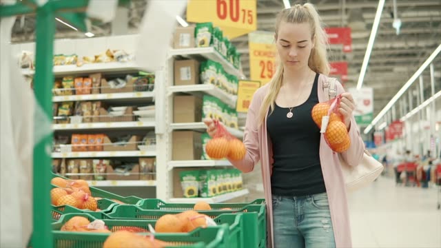 Young-blonde-woman-is-taking-packages-with-oranges-in-a-supermarket