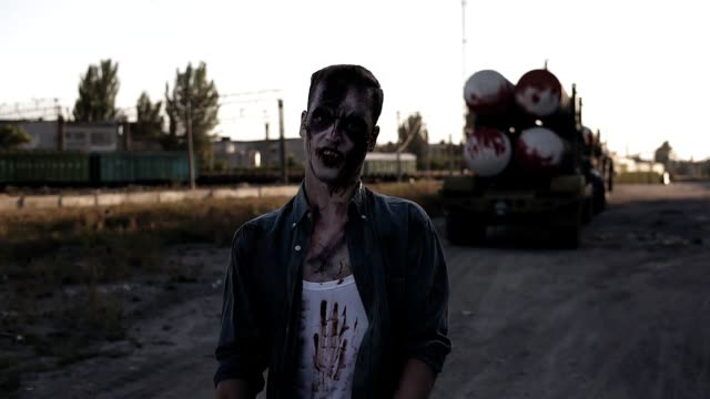 Creepy-zombie-man-with-clawing-hands-walking-outdoors-with-an-industrial-abandoned-place-on-the-background.-Halloween,-filming,-creepy-concept