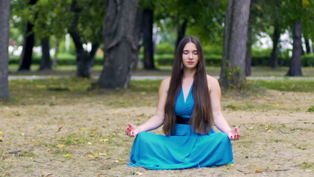 Schöne-Frau-im-blauen-Kleid-in-Lotus-stellen-meditieren-im-Park,-langsame-Dolly-Pfanne