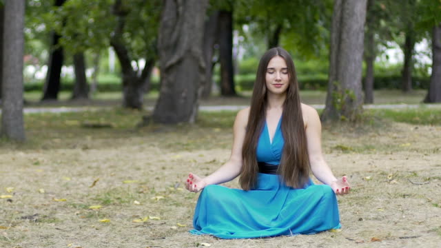 Beautiful-woman-in-blue-dress-meditates-outdoors,-place-for-ad-text,-dolly-shot