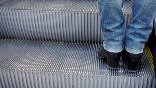 Frauen-die-Beine-in-Stiefeln-und-Jeans,-die-Rolltreppe-hinauf.