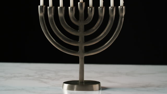 Tilt-shot-of-Jewish-menorah-candelabrum-with-lit-candles-on-a-grey-marble-surface,-against-black-background