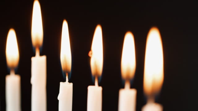 Close-up-of-six-lit-white-candles-burning-in-a-row,-rack-shot