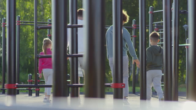 Sportliche-Eltern-Wandern-mit-Kindern-am-Spielplatz-im-Freien-Training