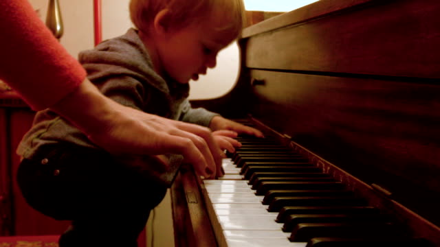 Caucásicos-niño-chico,-sentado-en-un-Piano-con-él-mamá,-juega-en-el-Piano-con-un-decorado-árbol-de-Navidad-detrás-de-ellos