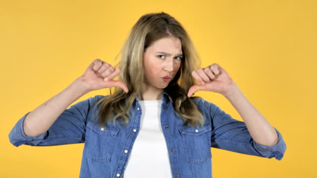 Portrait-of-Young-Pretty-Girl-Gesturing-Thumbs-Down-on-Yellow-Background