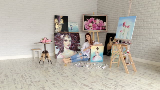 Una-artista-talentosa-chica-se-sienta-en-el-piso-entre-los-muchos-de-sus-cuadros.