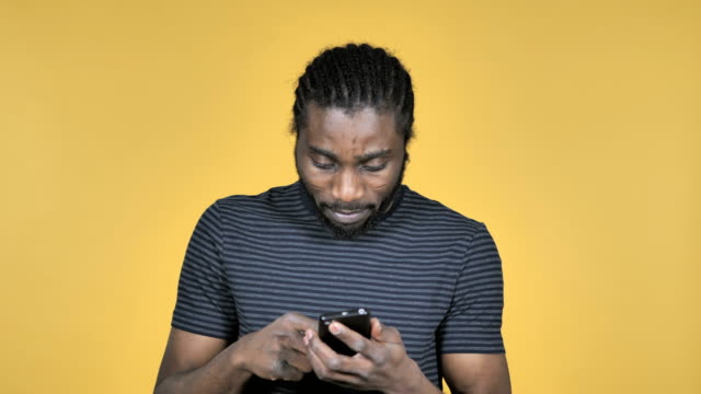 Online-Shopping-on-Smartphone-by-Casual-African-Man-Isolated-on-Yellow-Background