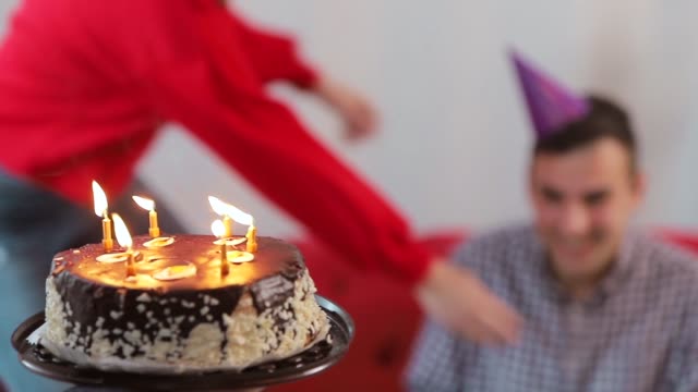 Handsome-man-blowing-birthday-candles-while-close-friends-throwing-a-surprise-party,-slowmotion-in-cozy-modern-apartment