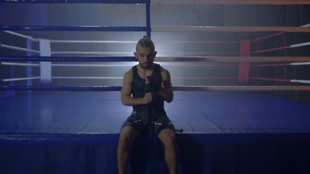 muskulöse-Wrestler-wickeln-schwarze-Bandagen-für-den-Boxsport-vor-Kampf-sitzen-in-der-Nähe-von-ring
